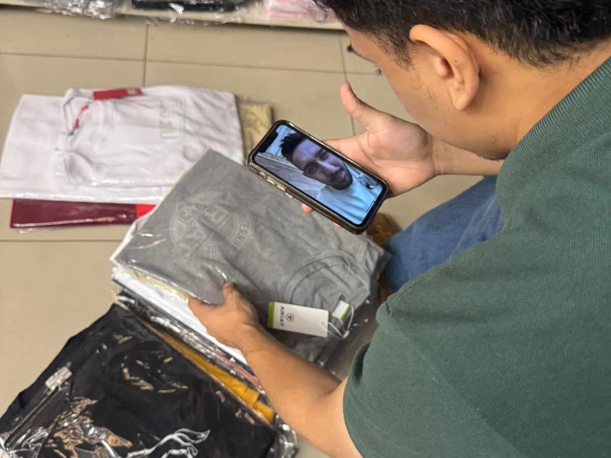 Vendedor mostrando uma peça masculina por chamada de vídeo no celular dentro da loja