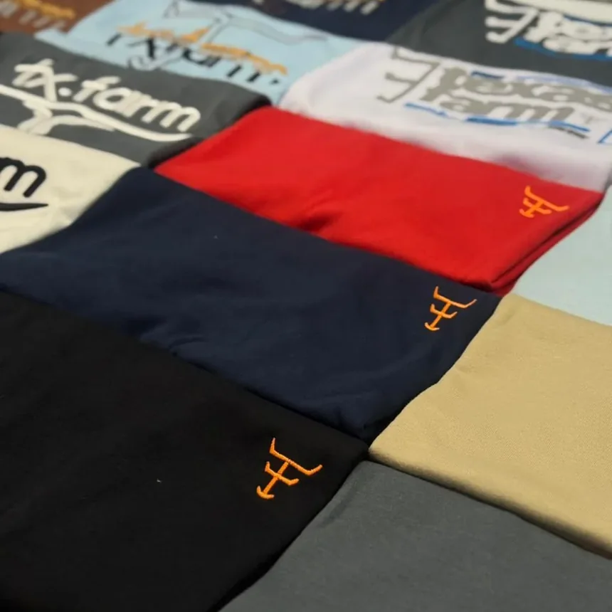Camisetas da DW Mens Wear dobradas em pilhas sobre a mesa da loja, prontas para o pedido de atacado